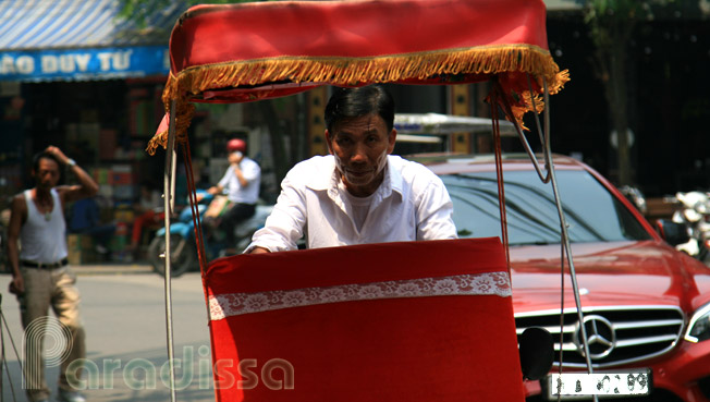 A cyclo driver in the Old Quarter by a luxurious car